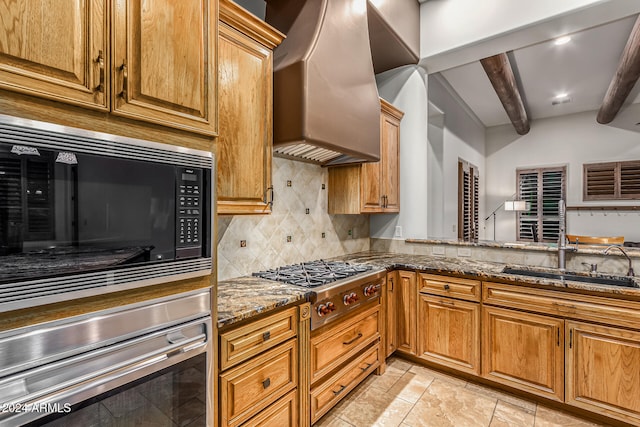 kitchen featuring beamed ceiling, custom range hood, stainless steel appliances, dark stone counters, and sink