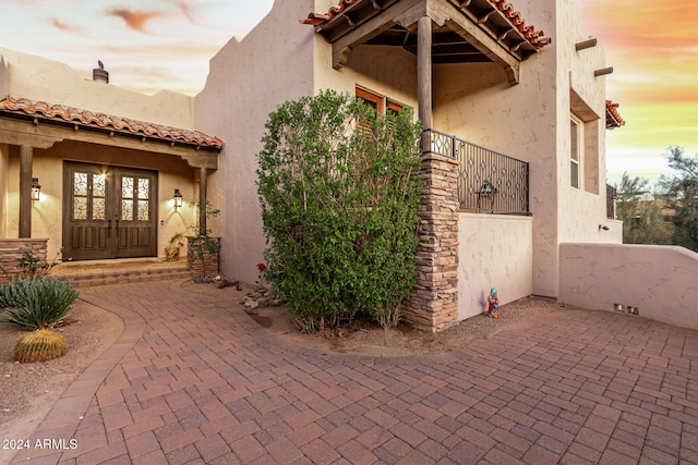 doorway to property featuring french doors, a tile roof, a patio area, and stucco siding