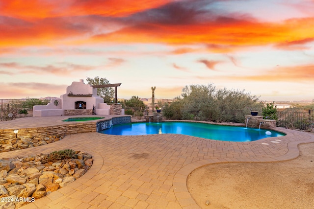 pool at dusk with a patio area, pool water feature, and exterior fireplace