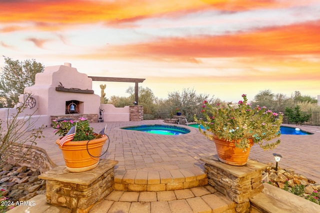 pool at dusk featuring an in ground hot tub, a fenced in pool, exterior fireplace, and a patio area