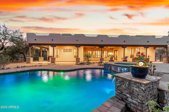 pool at dusk with a ceiling fan, a pool with connected hot tub, and a patio area