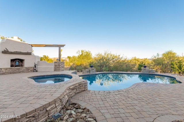 pool with an outdoor fireplace, an in ground hot tub, and a patio area