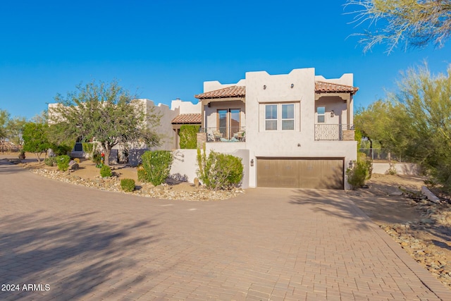 pueblo-style house with decorative driveway, an attached garage, a tile roof, and stucco siding