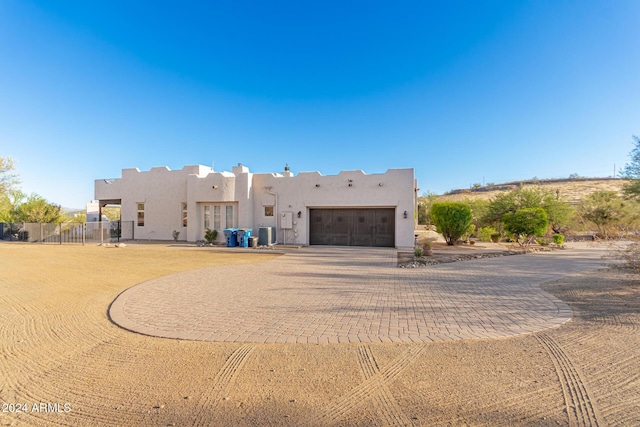 pueblo-style home featuring central AC unit, a garage, decorative driveway, fence, and stucco siding