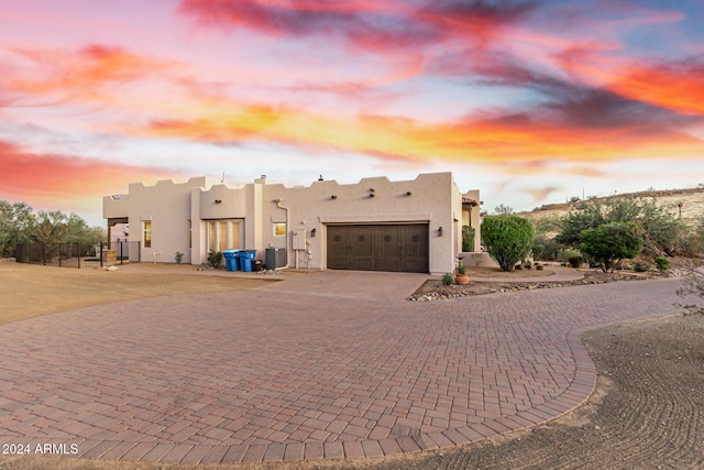 pueblo-style home featuring fence, an attached garage, stucco siding, central AC unit, and curved driveway