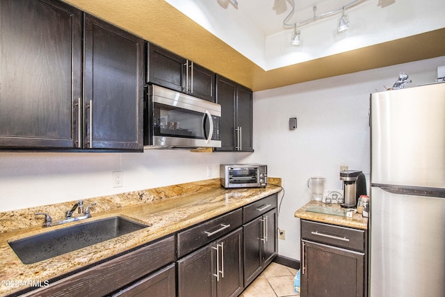 kitchen featuring light stone counters, a toaster, light tile patterned floors, stainless steel appliances, and a sink