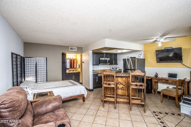 bedroom with light tile patterned flooring, visible vents, a textured ceiling, and freestanding refrigerator