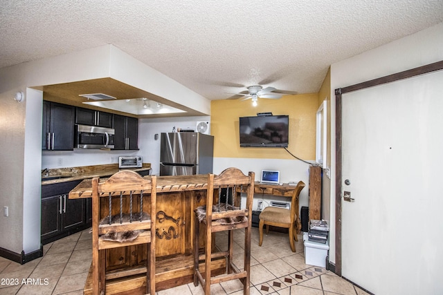 kitchen with light tile patterned floors, a textured ceiling, stainless steel appliances, and dark cabinets