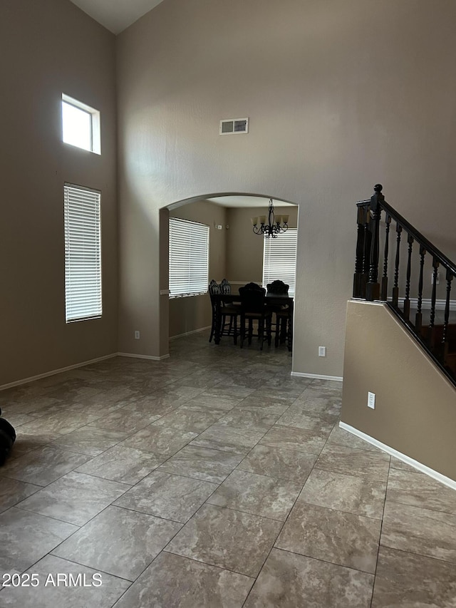 interior space featuring visible vents, baseboards, a chandelier, a high ceiling, and arched walkways