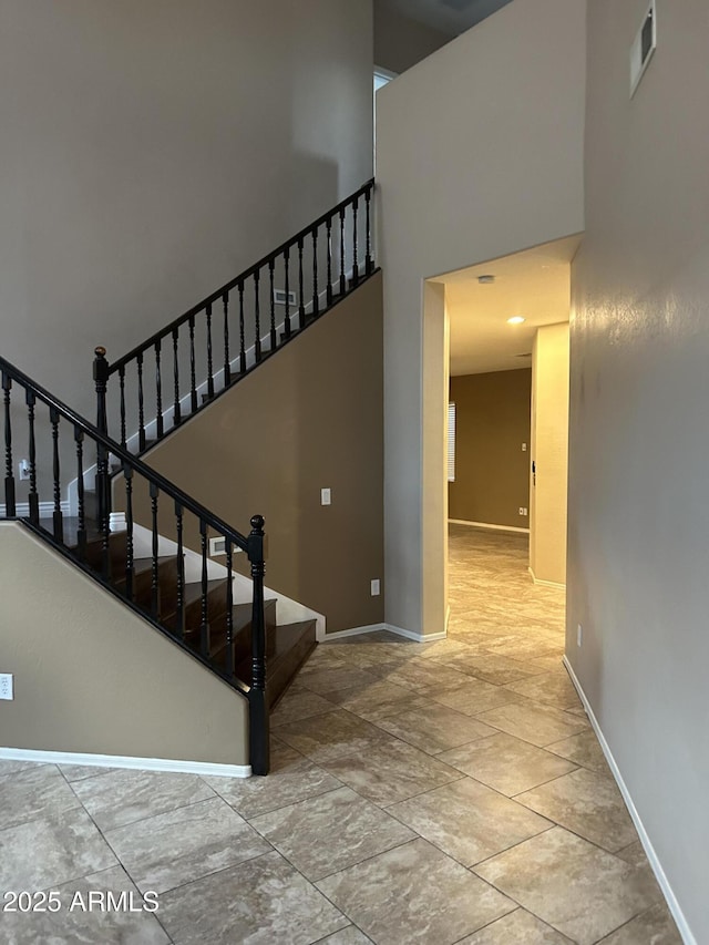 staircase featuring a high ceiling, baseboards, and visible vents