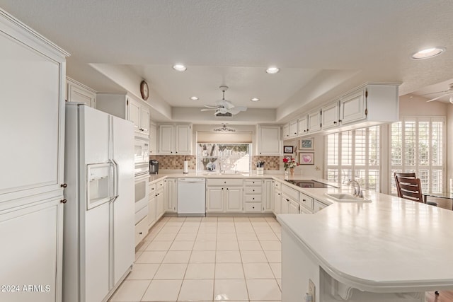 kitchen featuring sink, tasteful backsplash, kitchen peninsula, white appliances, and white cabinets