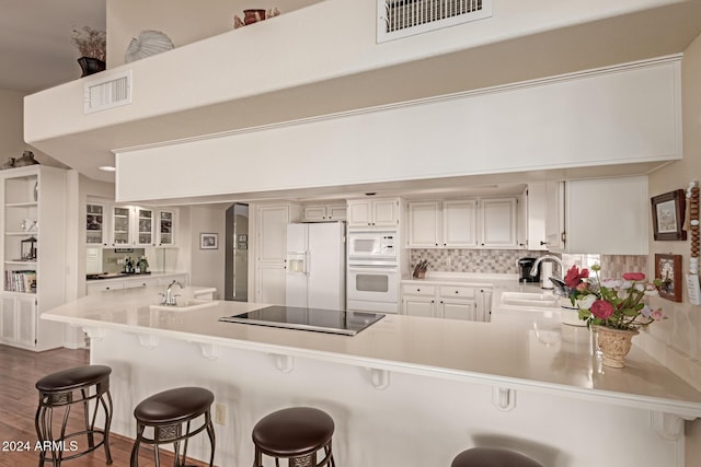 kitchen featuring sink, dark hardwood / wood-style flooring, kitchen peninsula, white appliances, and a breakfast bar area