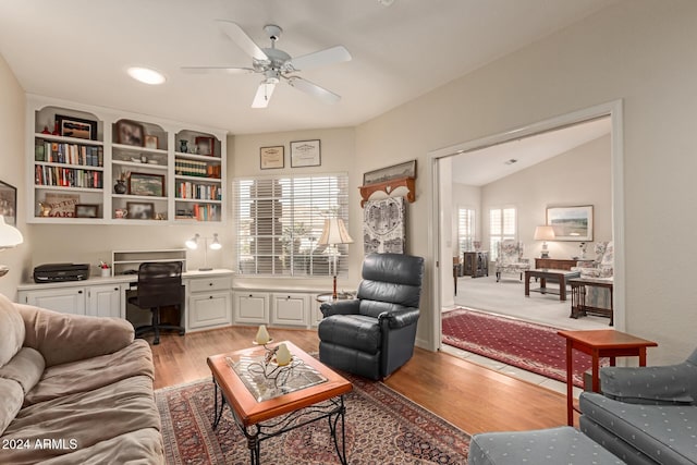 interior space with ceiling fan, vaulted ceiling, built in desk, and light hardwood / wood-style flooring