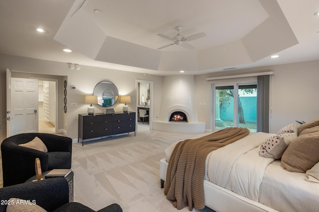 carpeted bedroom with ensuite bath, a large fireplace, a raised ceiling, ceiling fan, and access to exterior