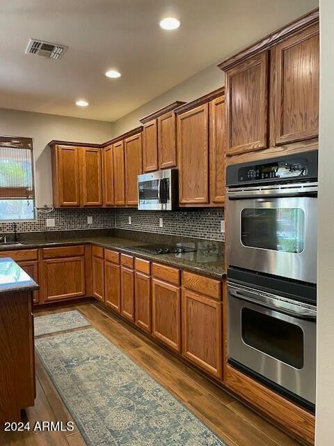 kitchen featuring tasteful backsplash, dark stone counters, stainless steel appliances, sink, and dark hardwood / wood-style floors