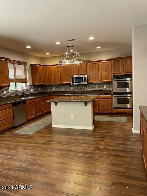 kitchen with a breakfast bar, dark wood-type flooring, decorative light fixtures, a kitchen island, and stainless steel appliances