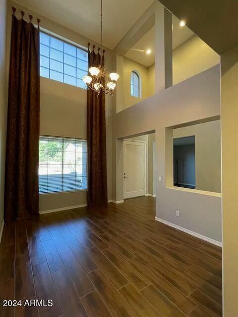 unfurnished living room featuring a towering ceiling, dark wood-type flooring, and an inviting chandelier