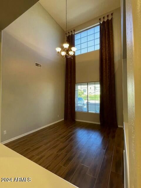 spare room with a high ceiling, an inviting chandelier, a wealth of natural light, and dark wood-type flooring