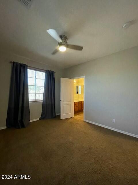 unfurnished bedroom featuring dark colored carpet, ceiling fan, and ensuite bathroom