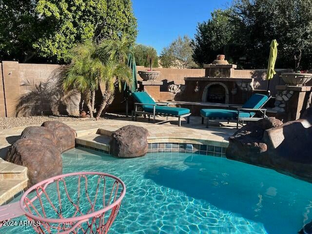 view of swimming pool featuring a patio area and exterior fireplace