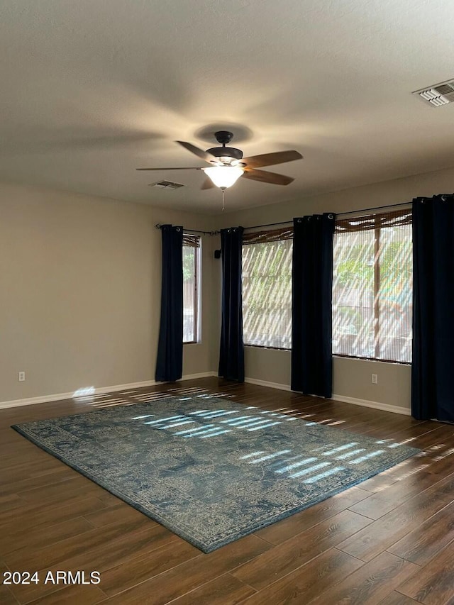 empty room with ceiling fan, a healthy amount of sunlight, and dark wood-type flooring