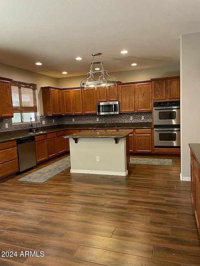 kitchen featuring a center island, a kitchen bar, hanging light fixtures, appliances with stainless steel finishes, and dark hardwood / wood-style flooring