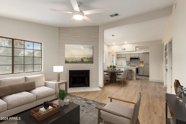 living room featuring a fireplace, ceiling fan, and light wood-type flooring