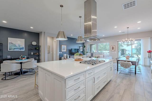 kitchen with island exhaust hood, a center island, decorative light fixtures, white cabinets, and stainless steel gas cooktop