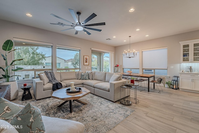 living room with ceiling fan with notable chandelier and light wood-type flooring