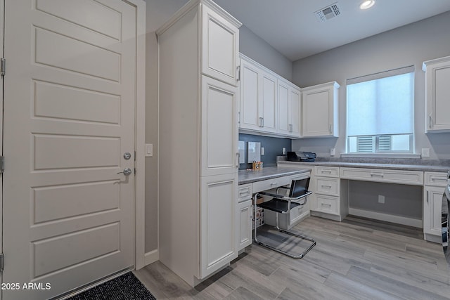 kitchen featuring white cabinets, light wood-type flooring, and built in desk