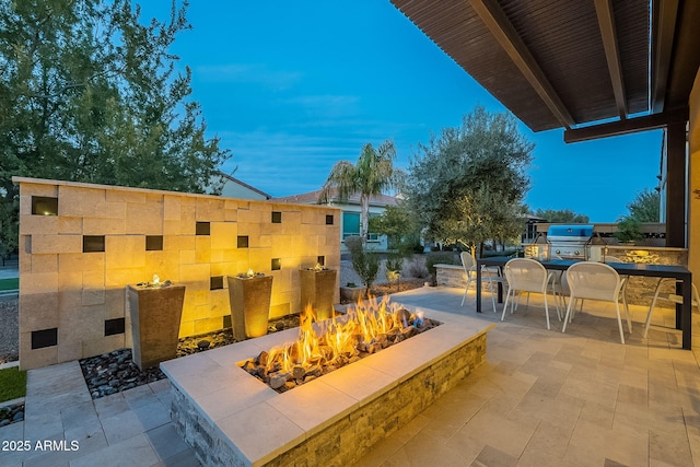 patio terrace at dusk featuring area for grilling, a grill, and a fire pit