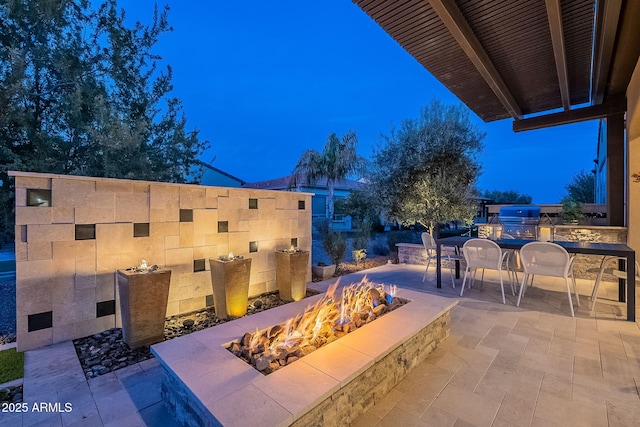 patio terrace at dusk with a grill, a fire pit, and exterior kitchen