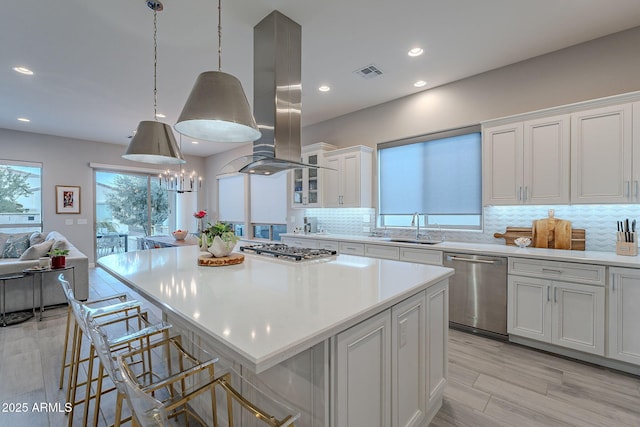 kitchen featuring stainless steel appliances, island exhaust hood, a center island, sink, and white cabinetry