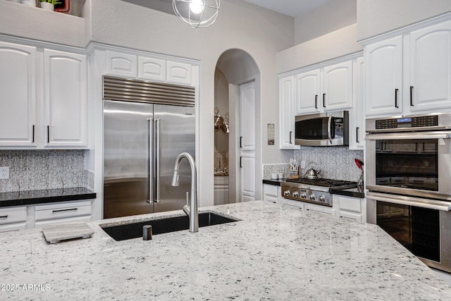 kitchen featuring stainless steel appliances, sink, white cabinets, and dark stone counters