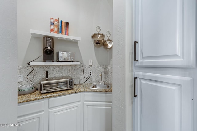 kitchen with white cabinetry, sink, backsplash, and light stone counters