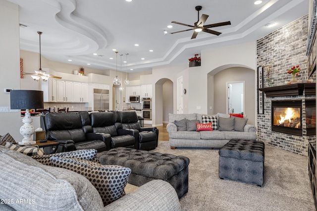 living room with ceiling fan, a large fireplace, and a raised ceiling