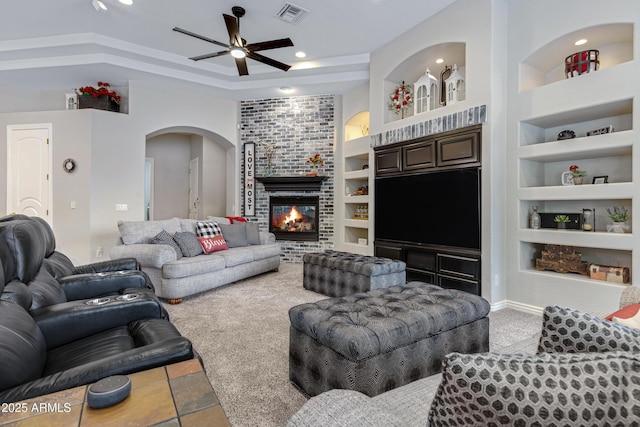 living room with built in features, ceiling fan, carpet flooring, a tray ceiling, and a fireplace