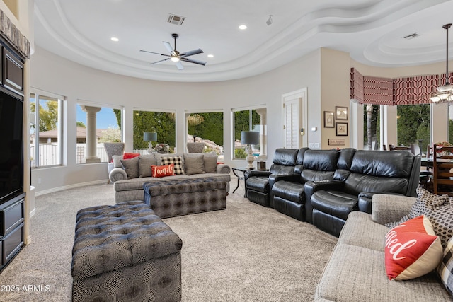 carpeted living room with a raised ceiling and ceiling fan with notable chandelier