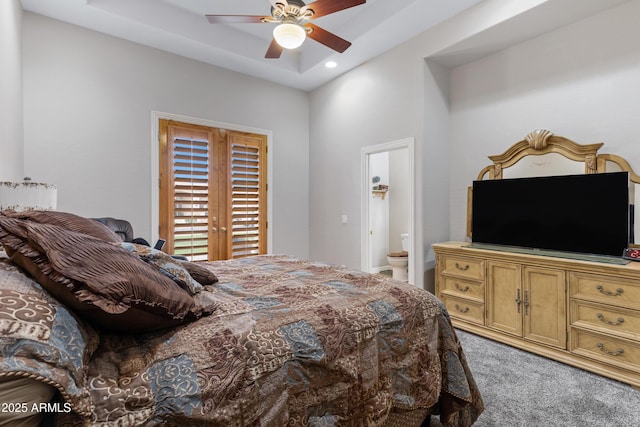 carpeted bedroom with a raised ceiling, ensuite bathroom, and ceiling fan