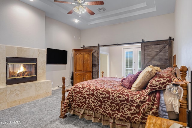 carpeted bedroom with ceiling fan, access to exterior, a fireplace, a raised ceiling, and a barn door