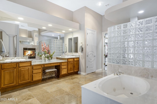 bathroom with a relaxing tiled tub, vanity, a tiled fireplace, and ornate columns