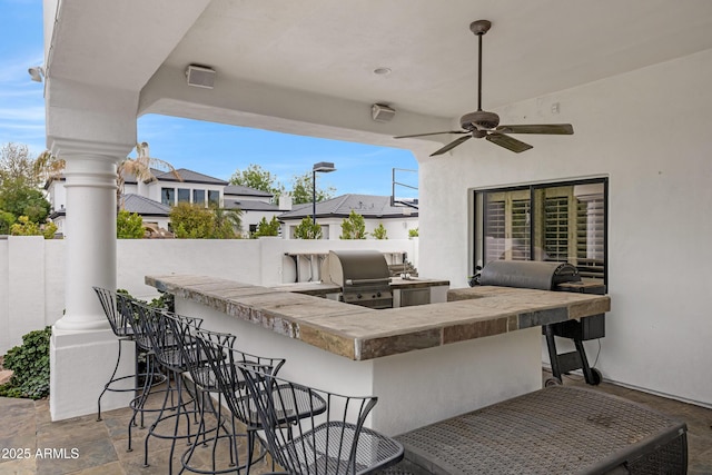 view of patio / terrace featuring a bar, ceiling fan, exterior kitchen, and area for grilling