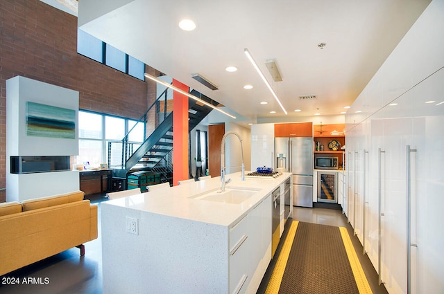 kitchen featuring light stone counters, white cabinets, sink, a kitchen island with sink, and appliances with stainless steel finishes