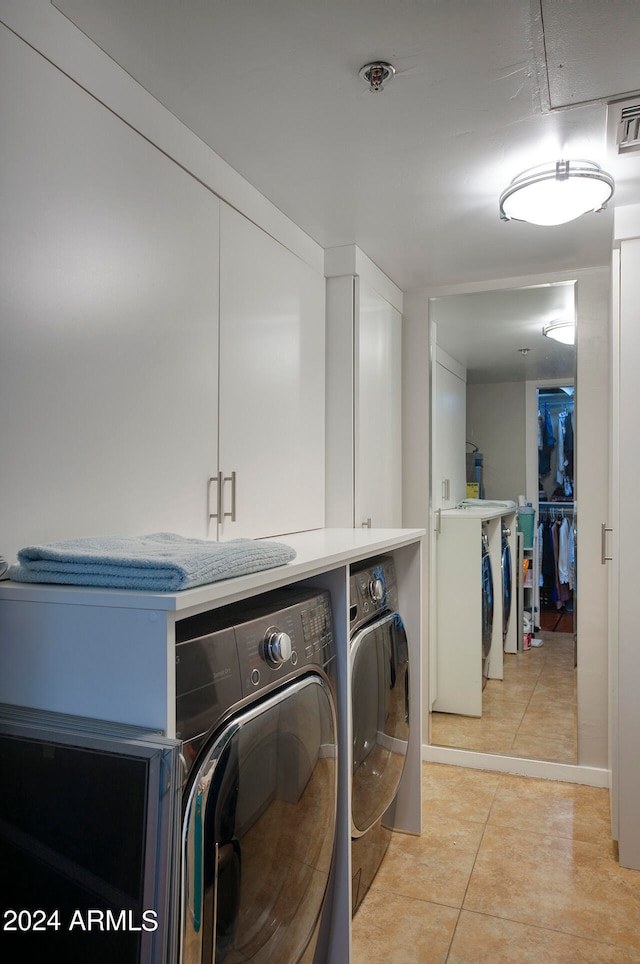 clothes washing area featuring cabinets, light tile patterned floors, and washing machine and clothes dryer