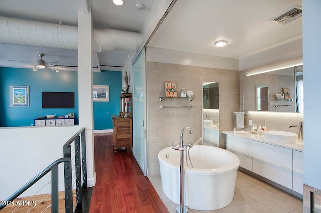 bathroom featuring wood-type flooring, tile walls, vanity, and a bathing tub