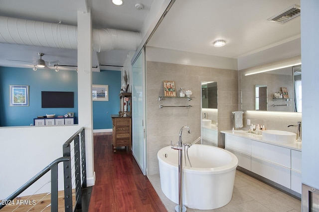 bathroom with a freestanding bath, tile walls, visible vents, ceiling fan, and vanity