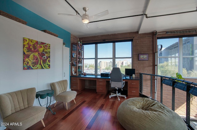 office featuring ceiling fan, a wealth of natural light, dark hardwood / wood-style floors, and brick wall