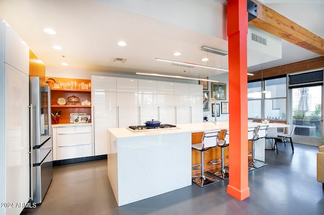 kitchen featuring white cabinets, appliances with stainless steel finishes, a kitchen bar, and beamed ceiling