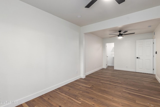 empty room featuring dark wood finished floors, a ceiling fan, and baseboards