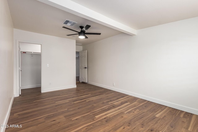 unfurnished bedroom featuring a spacious closet, visible vents, dark wood-type flooring, baseboards, and beam ceiling